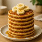 Fluffy banana pancakes topped with sliced bananas and syrup